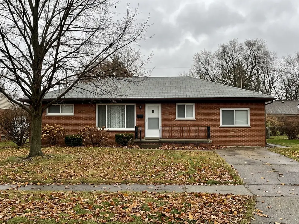 Low brick ranch house with a flat grey three-tab asphalt shingle roof, even rows of cutouts, under a bare maple in late autumn