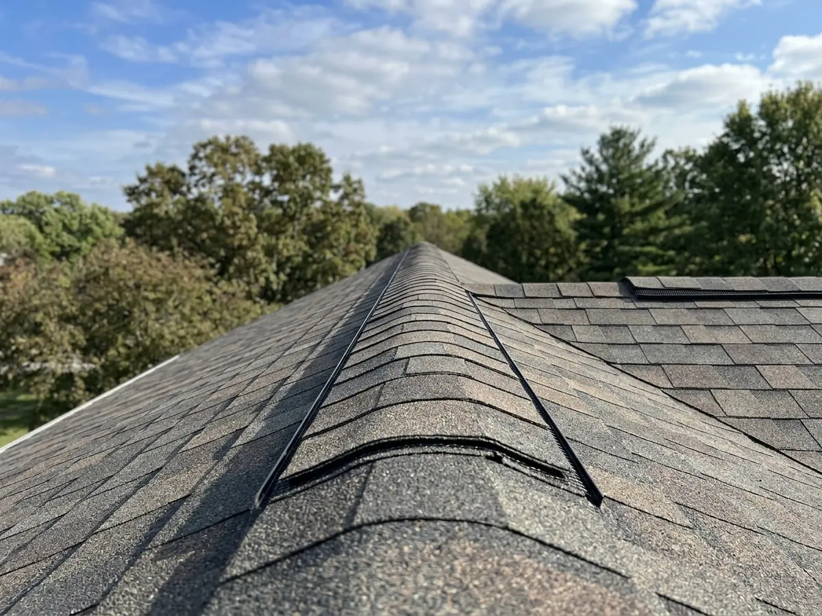 Continuous shingle-over ridge vent running the length of a newly shingled roof peak against a blue sky