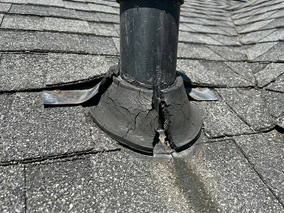 Cracked and split rubber collar of a pipe boot around a plumbing vent stack on a dark shingle roof