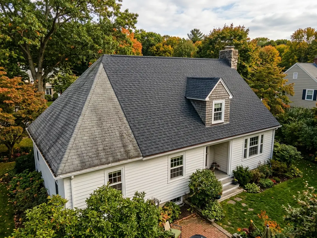 Rear slope of a two-story house with new grey shingles meeting older weathered shingles at the ridge